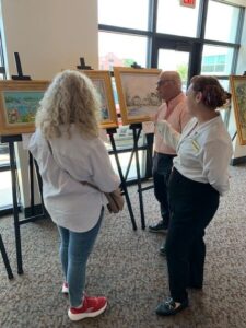 Three people viewing paintings in gallery.