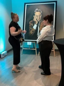 Two women discussing a large framed portrait.