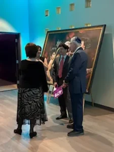 People conversing near large painting in gallery.